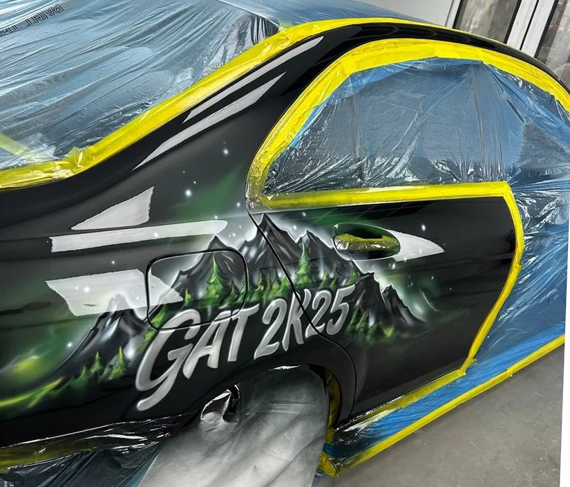 Snowmobile cowl airbrushed with mountains and custom lettering, masked mid-job