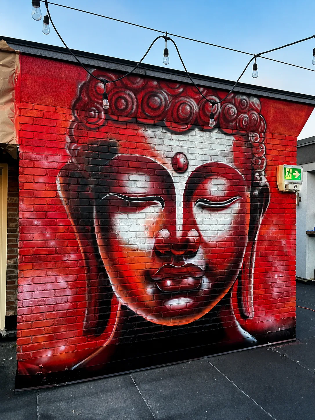 Red Buddha mural on exterior brick, patio setting