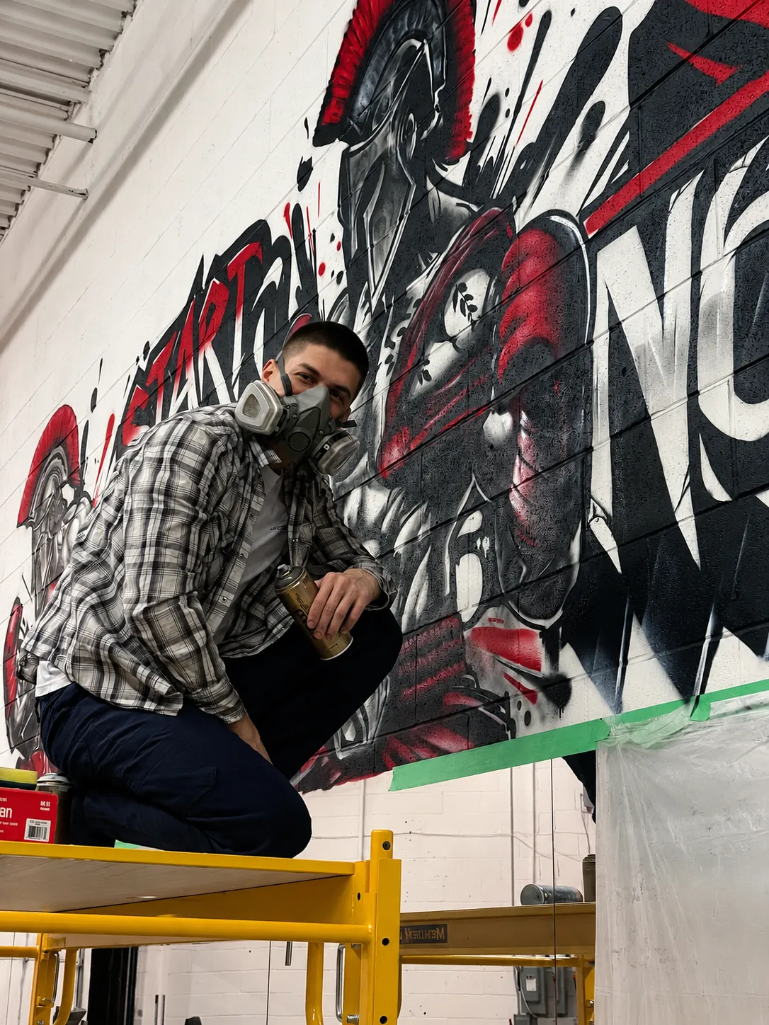 Kostya in a respirator on a scaffold lift, painting a mural
